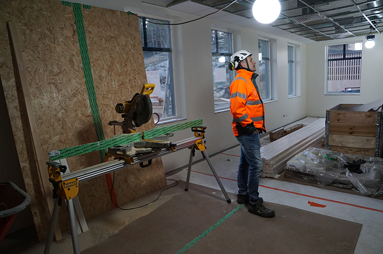 en man i orange varselkläder och hjälm står inne i byggnaden, det pågår byggarbete 