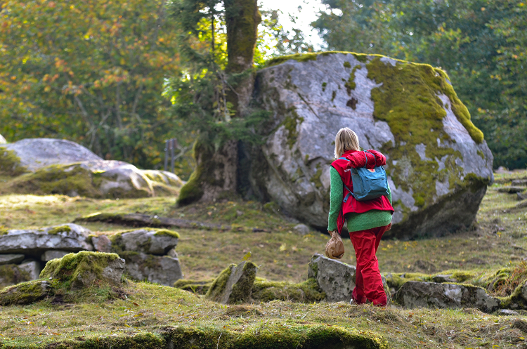 Kvinna vandrar i vacker miljö med en stor sten som är täckt med mossa