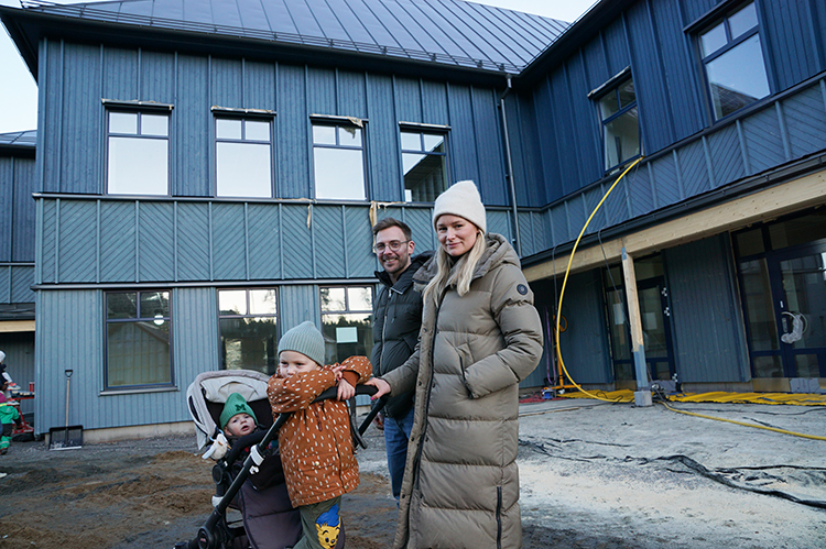 En man och en kvinna som står framför nya förskolan med en barnvagn med två nyfikna barn. 