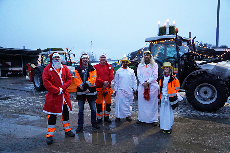 Glada luciaklädda medarbetare står framför traktorer med julbelysning
