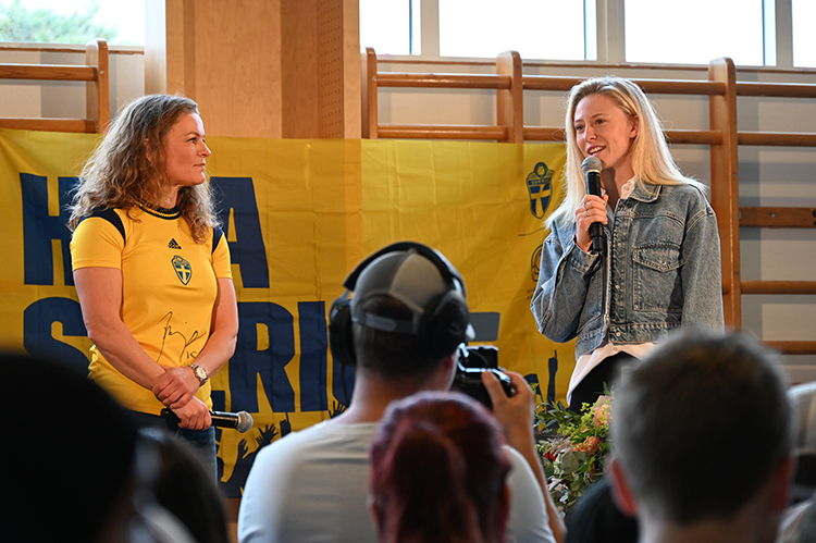 Malin Krantz och Rebecka Blomqvist står på en scen och Rebecka pratar i en mikrofon