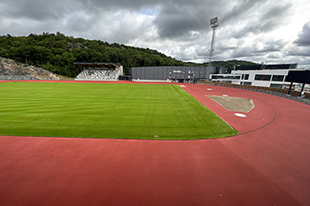 Rimnersvallens röda löparbanor, fotbollsplan och östra läktaren syns, liksom Rimnershallen och bygget av Rimnersbadet. 