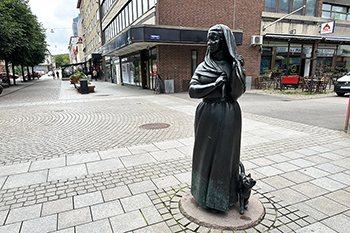En skulptur av en kvinna med förkläde och sjalett, hon har en katt vid sin ena sida