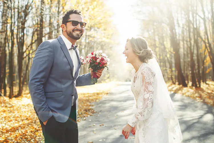 ett brudpar med en man i grå kostym och en kvinna i vit bröllopsklänning som ser glada ut