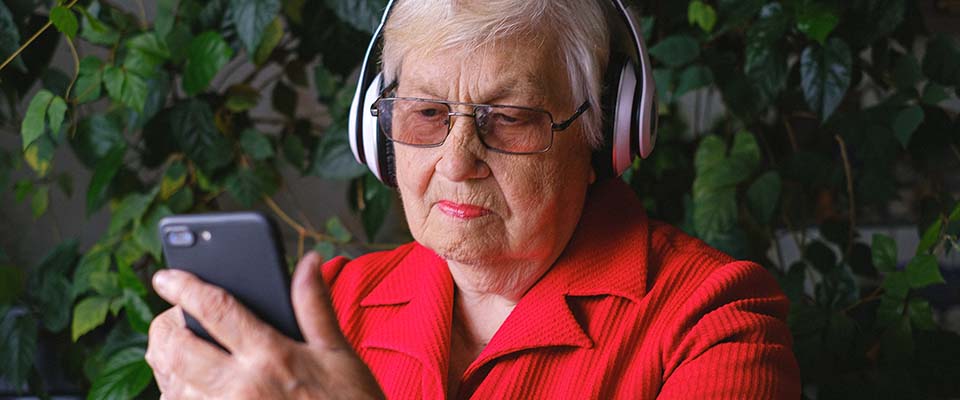 Äldre kvinna med hörlurar använder en smartphone