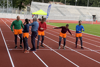 Några män och kvinnor i orange shorts och träningskläder står i startgroparna för att springa och blir intervjuade