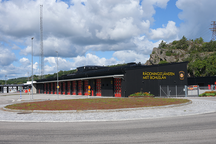 Bild på Uddevallas mnya bradnstation som är svart och har röda garageportar samt texten Räddningstjänsten Mitt Bohuslän