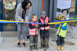 tre barn står tillsammans med förskolepersonal och klipper ett blågult band framför entrén till en blå byggnad