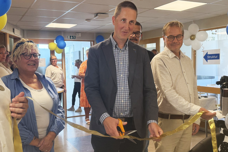 Tre personer klipper ett gult band med guldsaxar. En skylt visar "Struktur".