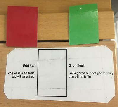 Bilden visar ett rött och ett grönt kort som eleven har på bänken för att visa om den vill vara ifred eller om det är fritt fram för pedagogen att gå fram.